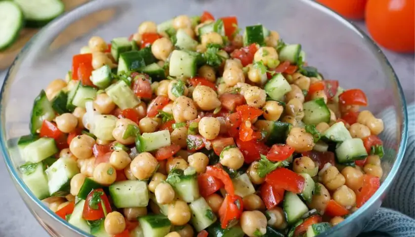 Frischer Kichererbsen Gurken Salat in einer Glasschüssel, garniert mit Petersilie und Tomaten.