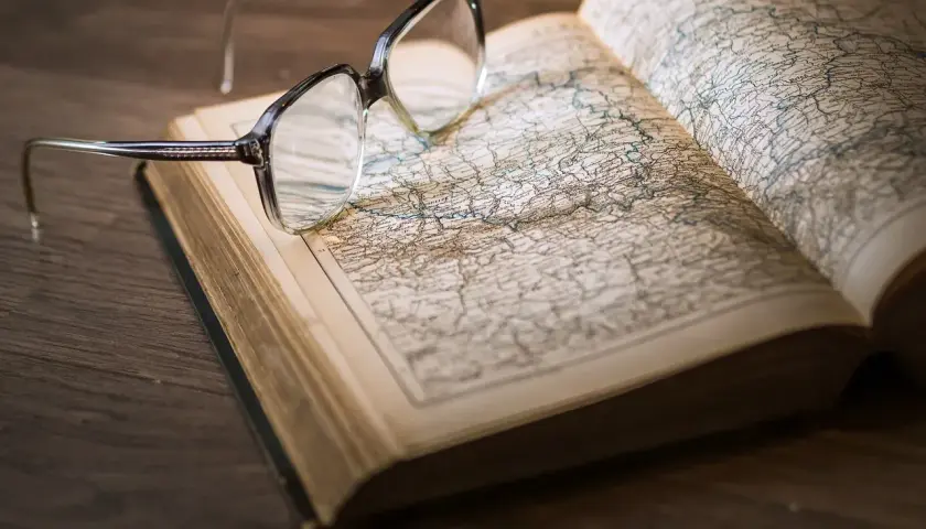 Okulary na otwartej księdze z mapą. Pomocne przy katalogowaniu źródeł i unikaniu błędów w researchu historycznym.