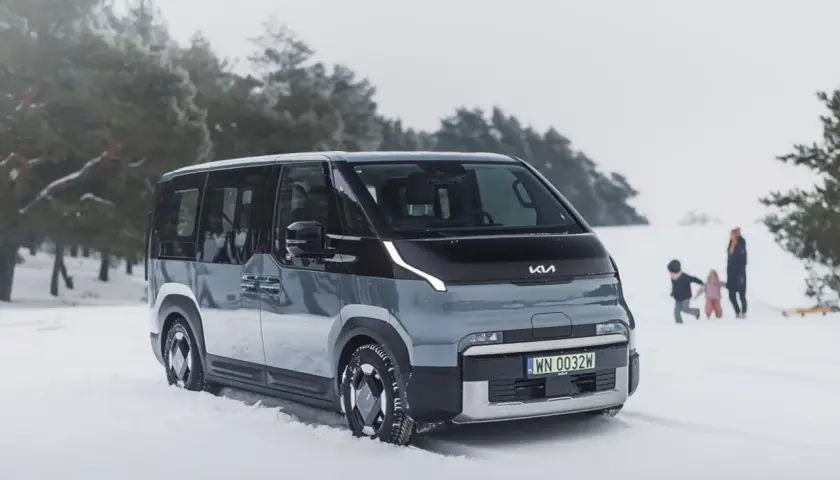 Nowy Kia PV5 w zimowej scenerii. Rodzina bawi się na śniegu w tle.