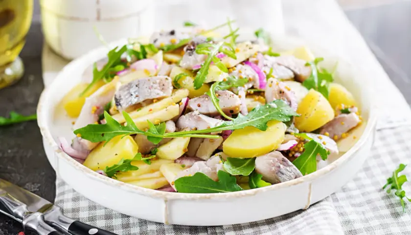 Salade de pommes de terre et hareng à l'huile, garnie de roquette et d'oignons rouges. Une recette simple et savoureuse.