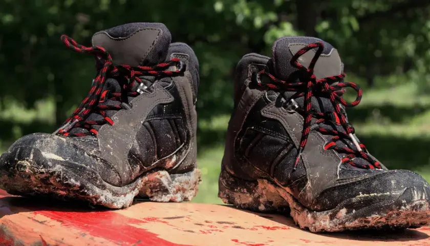 Mud-caked hiking boots with red and black laces sit on a red surface. These boots show signs of heavy use, hinting at how long do hiking boots last.