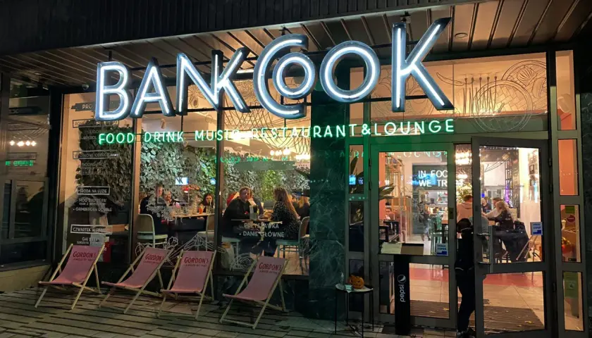 Klimatyczne restauracje Poznań: neonowy szyld "BANKOOK" nad wejściem, w środku ludzie przy stolikach.
