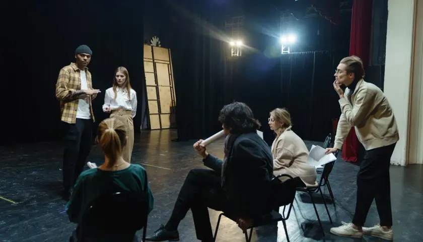 Grupa ludzi na scenie, dyskutująca o sztuce. Zastanawiają się, ile zarabia reżyser w Polsce, analizując scenariusz.
