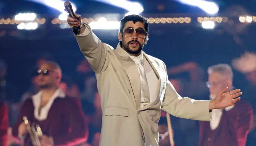 Bad Bunny koncert: artysta w beżowym garniturze z mikrofonem w dłoni, na scenie z tłumem w tle.
