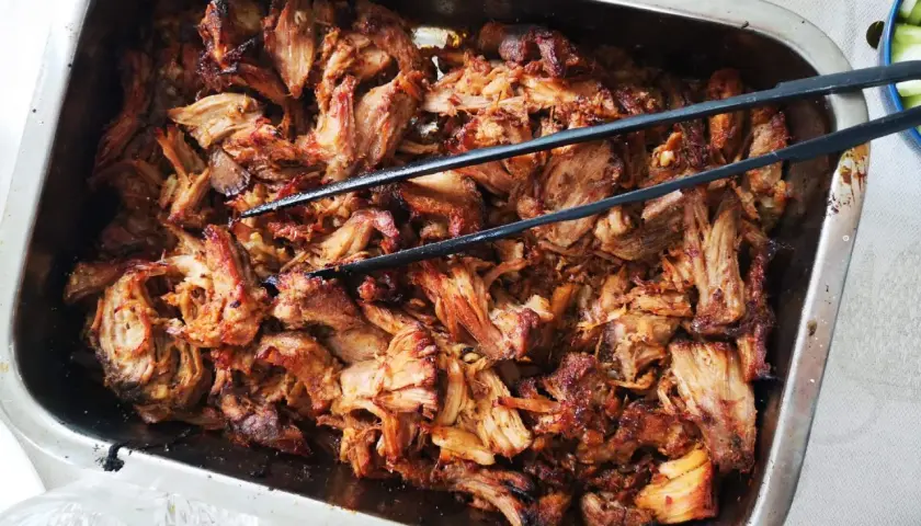 Saftigt, strimlat fläskkött i en ugnsform, redo att serveras. Perfekt för ett gott carnitas recept!