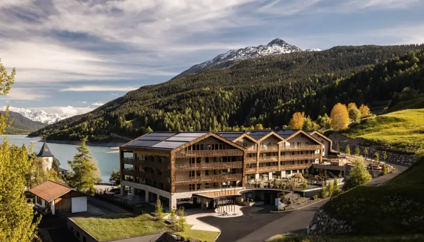 Das Gerstl Family Retreat, un hotel moderno con pannelli solari, si affaccia su un lago alpino e montagne boscose.