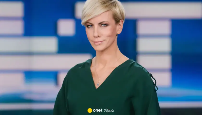 Anita Werner w zielonej sukience, z krótkimi blond włosami, na tle niebiesko-białej grafiki.