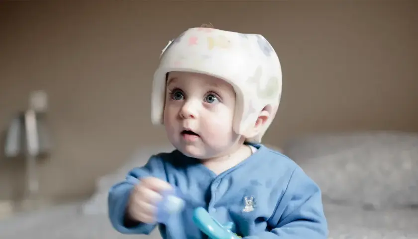 Niebieskooki maluch w kolorowym kasku korekcyjnym z zabawką w ręku.