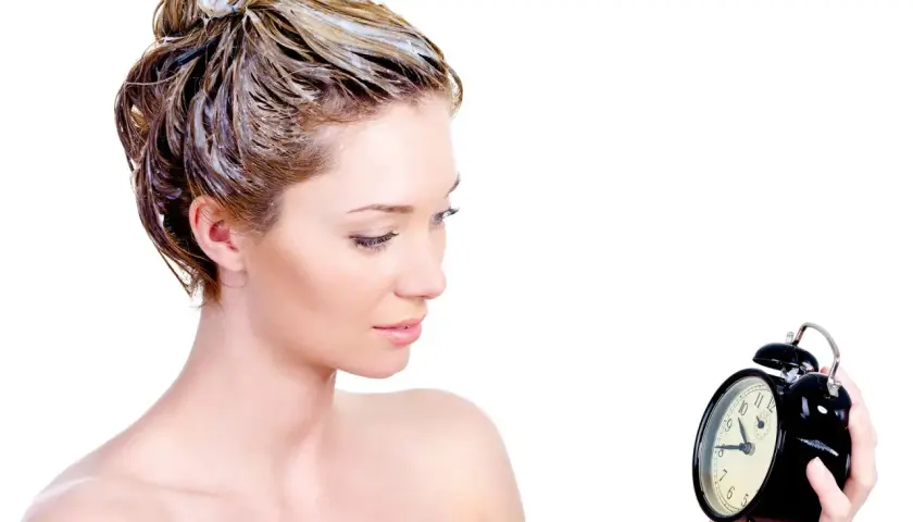 Mujer con tinte en el pelo, mirando un reloj. El tiempo es crucial para un tinte pelo perfecto.