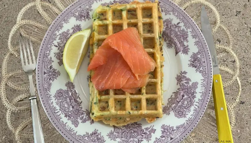 Gaufres salées garnies de saumon fumé et d'un quartier de citron, sur une assiette ornée, avec une fourchette et un couteau à manche jaune.