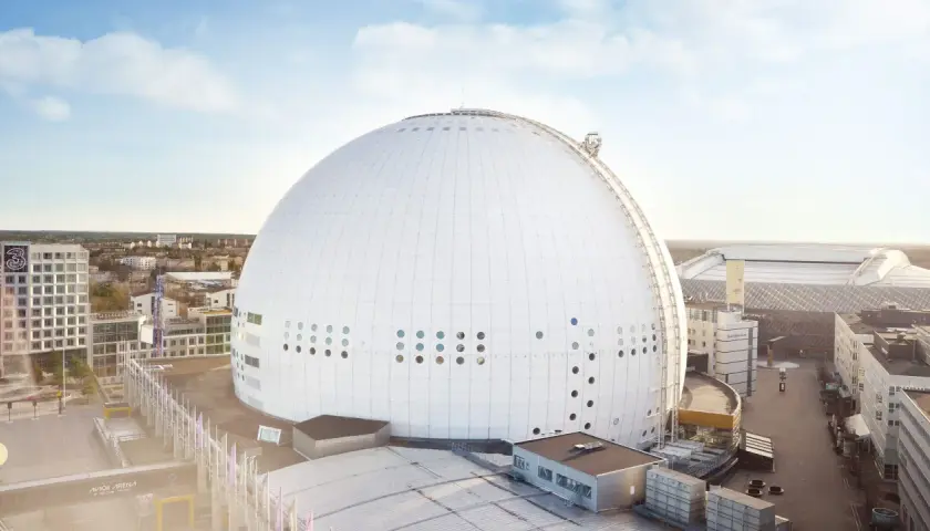 En solig dag vid Globen, Stockholm. Den ikoniska sfäriska arenan dominerar landskapet, omgiven av moderna byggnader och en klarblå himmel.