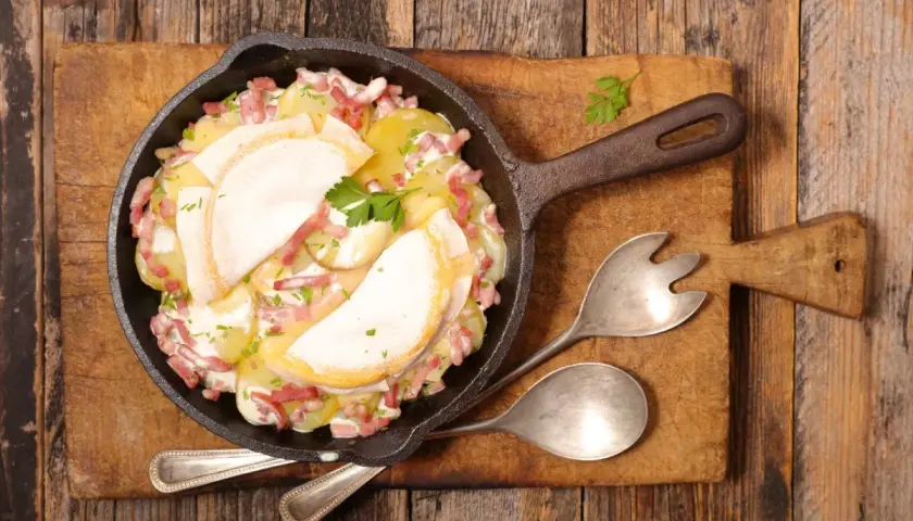 Plat de pommes de terre gratinées avec lardons et fromage fondant, servi dans une poêle en fonte. Un plat avec charcuterie réconfortant.