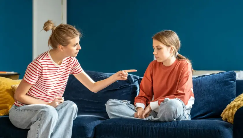 Matka z wyrzutem wskazuje palcem na córkę, która siedzi z opuszczoną głową. Scena sugeruje odrzucenie matki przez dorosłe dziecko.