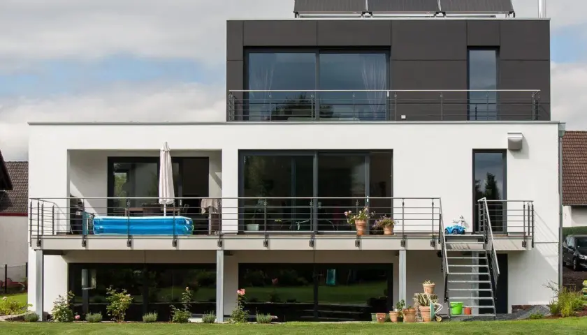 Moderne Hausumbau-Ideen: Vorher-Nachher-Vergleich eines weißen Hauses mit dunklem Anbau, Balkon und Pool.