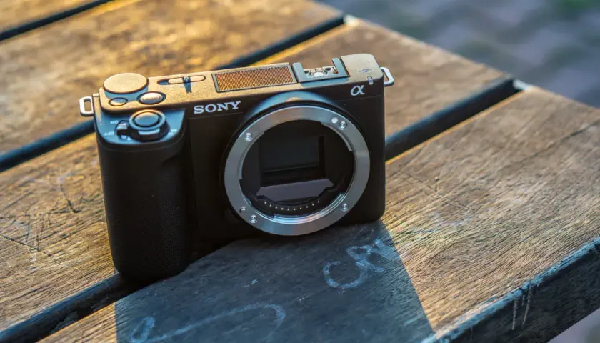 Czarny aparat Sony ZV-E10 II bez obiektywu leży na drewnianym stole, oświetlony ciepłym, zachodzącym słońcem.