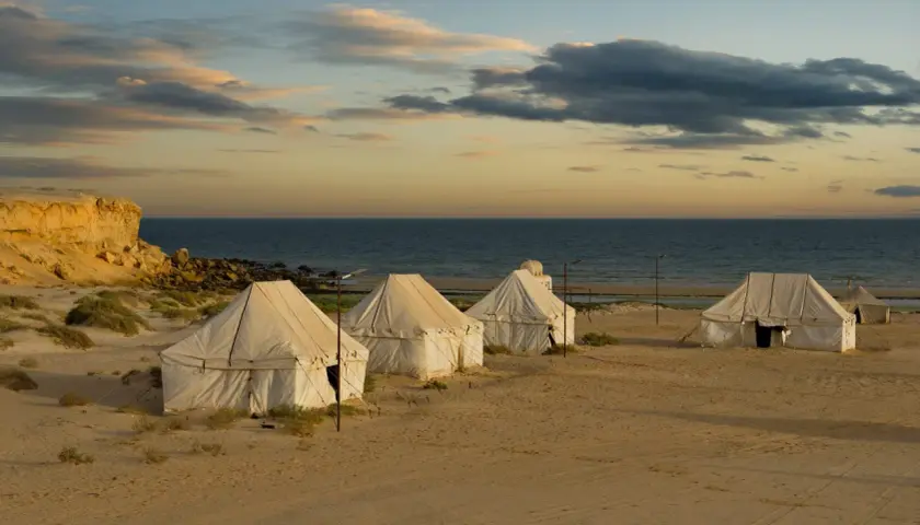 Namioty na piaszczystej plaży nad oceanem o zachodzie słońca.