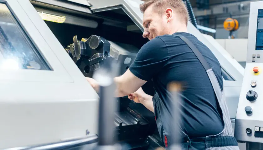 Operator CNC w kombinezonie pracuje przy maszynie, regulując jej elementy.
