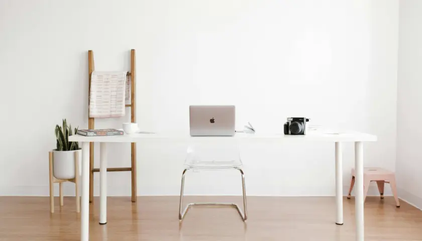 Ein moderner Arbeitsplatz mit einem weißen Schreibtisch, Laptop, Kamera und einer Pflanze. Perfekt für alle, die einen **tisch selber bauen** möchten.