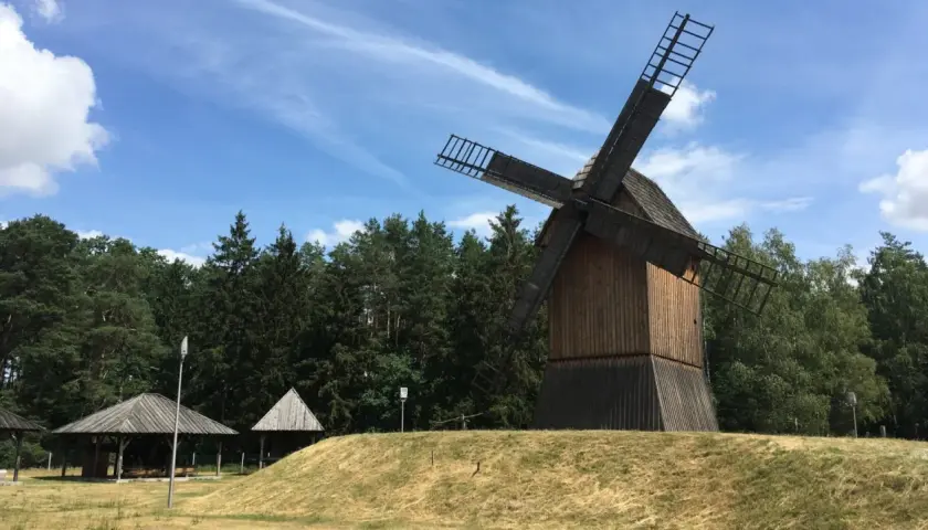 Drewniany wiatrak na wzgórzu, otoczony lasem, w tle błękitne niebo z chmurami. Miejsce jak z bajki w Obornikach Śląskich.