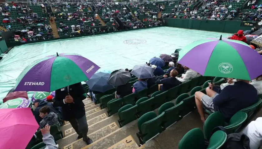 Wimbledon deszcz przerwał mecz. Widzowie siedzą pod parasolami, a kort przykryty jest plandeką.