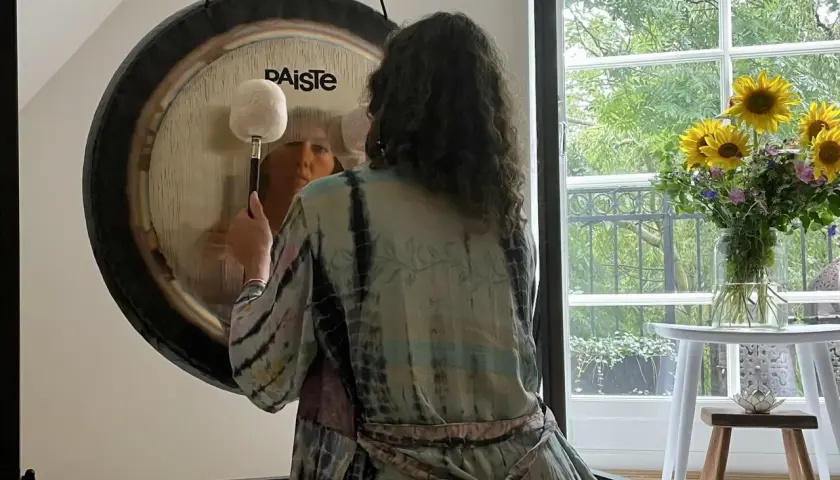 Person i färgglad kimono förbereder sig för gong bad. En stor gong står framför ett fönster med solrosor.