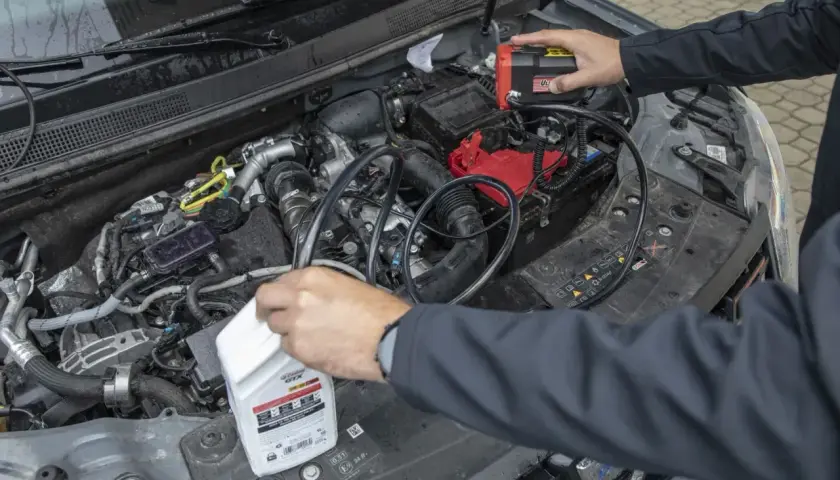 Mechanik próbuje zdiagnozować za wysoki poziom oleju w silniku diesla, podłączając urządzenie do akumulatora i trzymając butelkę oleju.