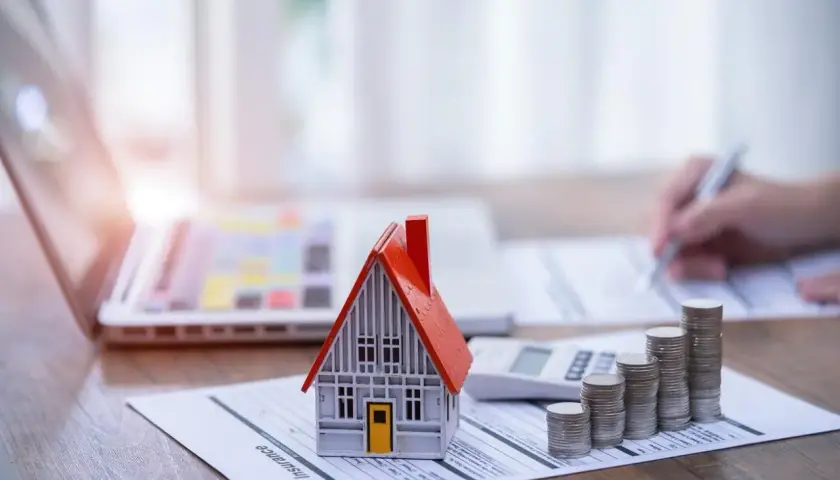 Model domu, stos monet i kalkulator na dokumencie "House Insurance". To symbol ubezpieczenia pomostowego, które chroni Twój dom.
