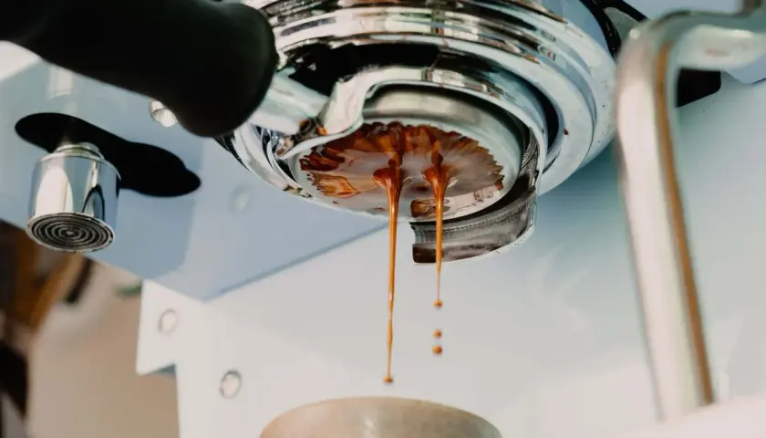Frisch gebrühter Espresso tropft aus der Siebträgermaschine. Der goldbraune Strahl deutet auf ein perfektes espresso ratio hin.