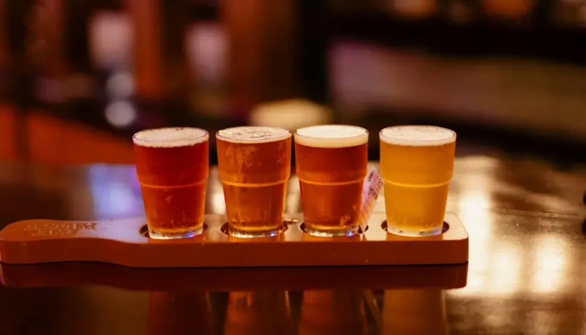Quatre verres de bière, de différentes couleurs, sur un plateau en bois. Une dégustation de bière, pas de bière chaude ici !