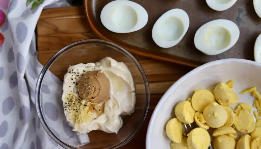 Ingredients for miso egg salad: mayonnaise, miso paste, pepper, and separated egg yolks in a bowl. Halved hard-boiled eggs are on a tray.