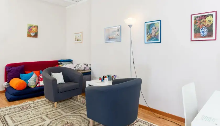 Accogliente studio psicologo in casa, con divano letto, poltrone, tappeto e quadri colorati.