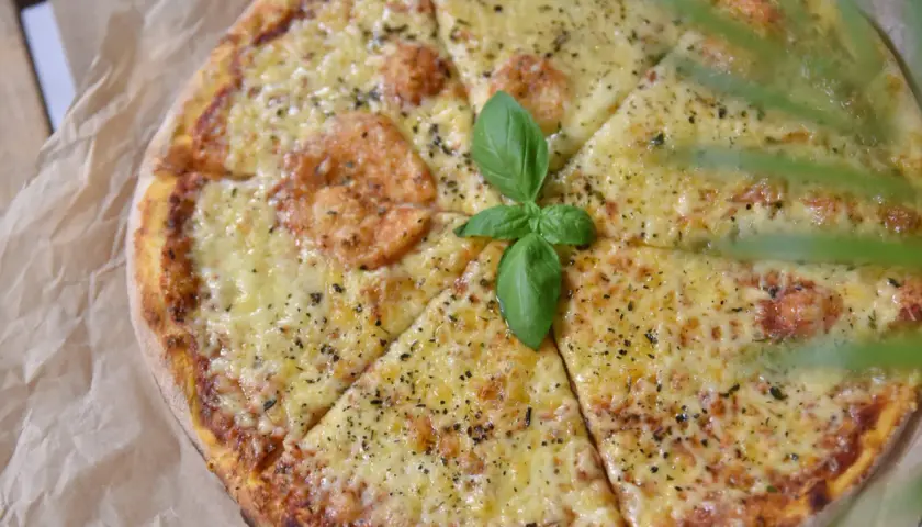 Pyszna pizza z roztopionym serem, posypana ziołami i udekorowana listkiem bazylii. Idealny ser do pizzy dla każdego smakosza.