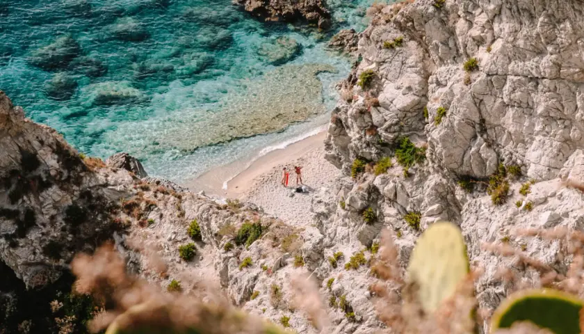 Malownicze kalabryjskie plaże z turkusową wodą i skalistymi klifami. Dwie osoby odpoczywają na piaszczystej plaży, ciesząc się słońcem.