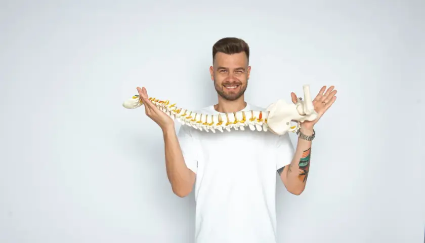 Uśmiechnięty mężczyzna trzyma model kręgosłupa, wyjaśniając, whiplash co to jest.