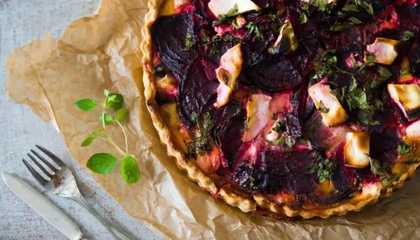 Apetyczna tarta buraczana z serem i ziołami, gotowa do podania. Obok sztućce i gałązka oregano.