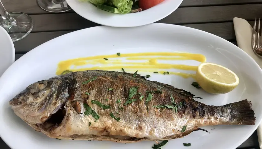 Dorade entière cuite à la plancha, servie avec une sauce jaune et un quartier de citron. Un plat savoureux, probablement mariné pour plus de goût.