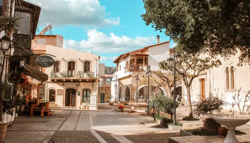 Malia, Kreta: malerische Gasse mit Cafés und traditionellen Gebäuden unter blauem Himmel.