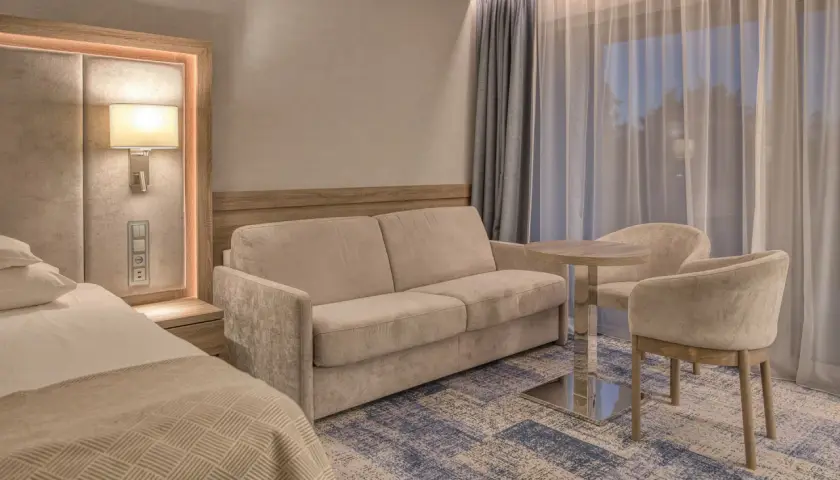 Przytulny pokój w hotelu 5 gwiazdkowym nad morzem: wygodna sofa, stolik z krzesłami i łóżko.