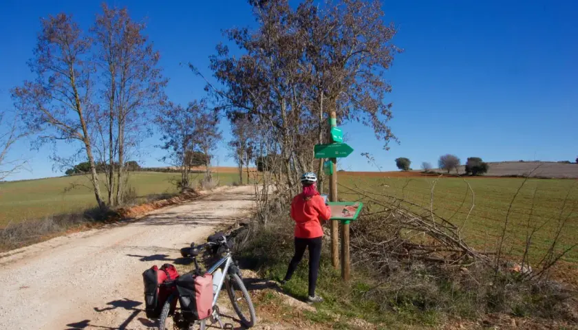 Ciclista consulta señalización en la **vía verde del Tajuña**. Bicicleta con alforjas lista para la aventura.