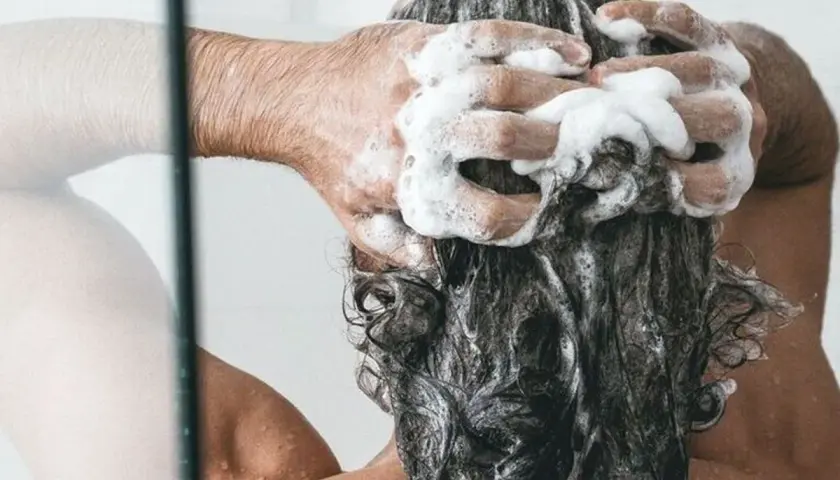 Persona disfrutando de un relajante lavado de cabeza con abundante espuma de champú.