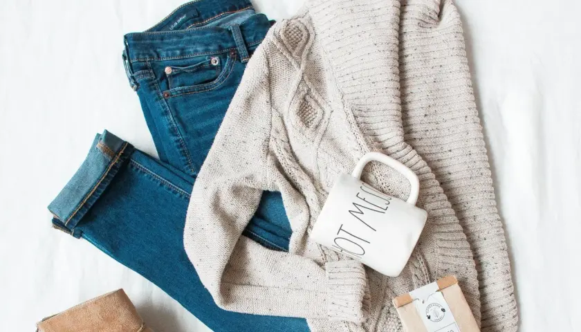 Un jean, un pull torsadé, une tasse et une botte en daim : un parfait style vestimentaire hiver pour une journée cosy.