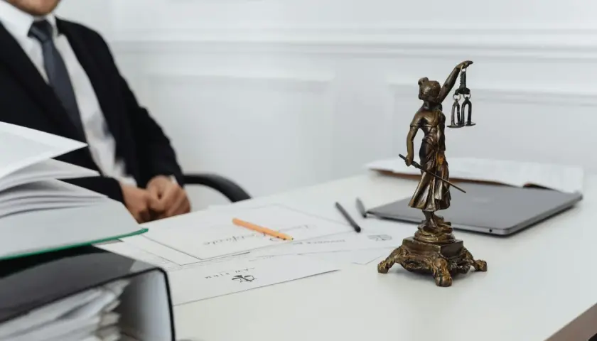 Une statue de la justice, symbole du juge de l'exécution, trône sur un bureau avec des documents et un homme en costume.