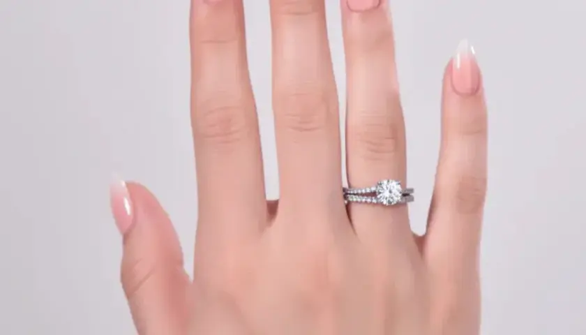 En hand med perfekt manikyr hemma visar upp en gnistrande diamantring och en matchande vigselring.