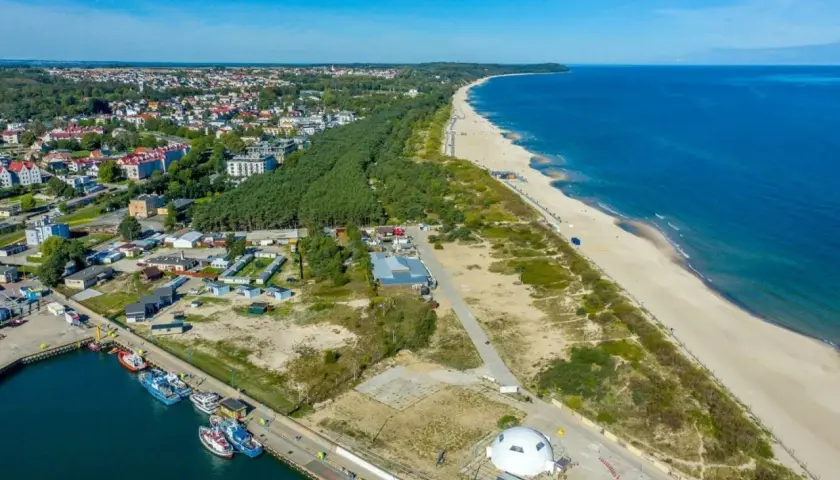 Widok na port i plażę w Władysławowie, z widoczną linią brzegową Jastrzębiej Góry w oddali.