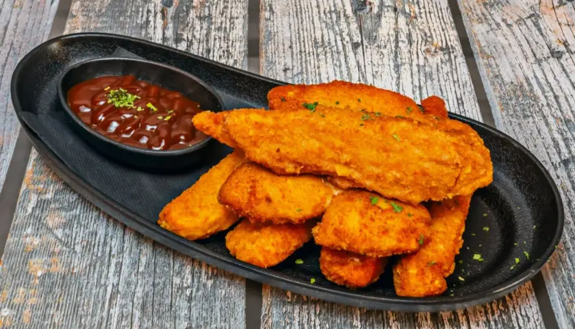 Chrupiący kurczak w panko, podany z sosem barbecue na czarnej tacy. Idealna przekąska.