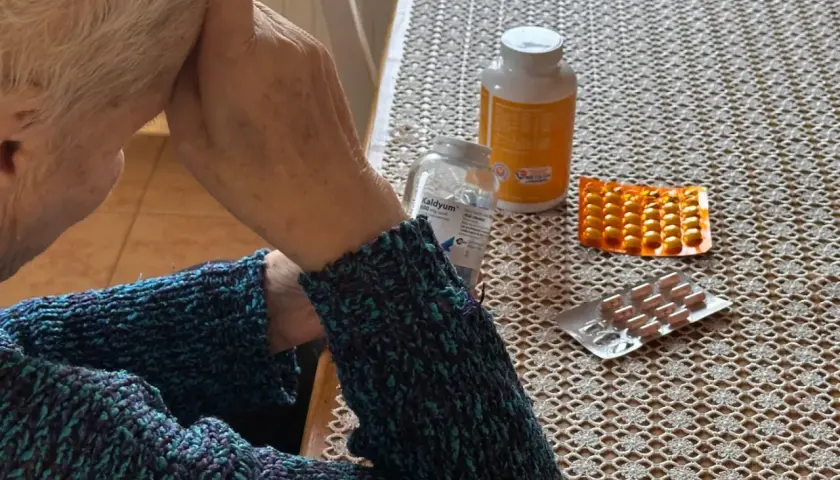 Osoba w swetrze z lekami na stole. Zastanawia się, renta wdowia komu przysługuje, szukając odpowiedzi.
