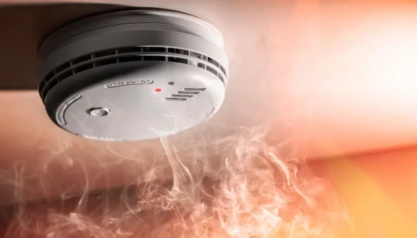 Detector de humo en el techo, rodeado de humo. Ilustra cómo funciona un detector de humo al alertar sobre el peligro.
