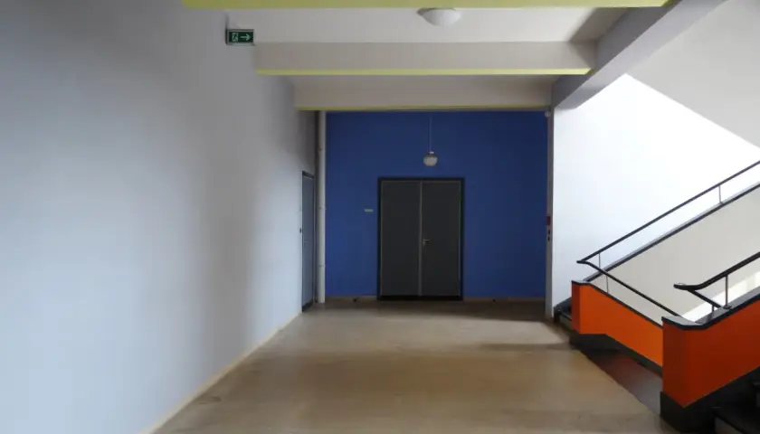 Ein Flur mit hellem Estrich, blauer Wand und auffälliger Treppe. Der Boden ist nach DIN-Norm verlegt.