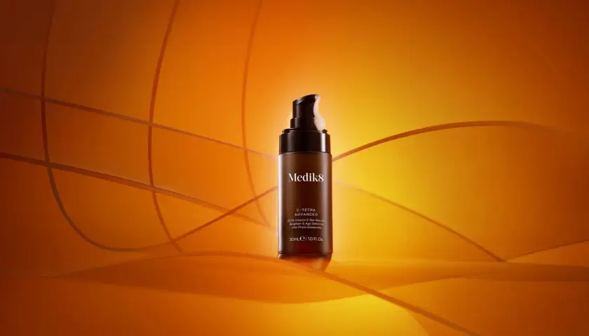 En flaska Medik8 C-Tetra Advanced serum med 20% C-vitamin, en kraftfull antioxidant för din hudvård, står på en orange bakgrund.