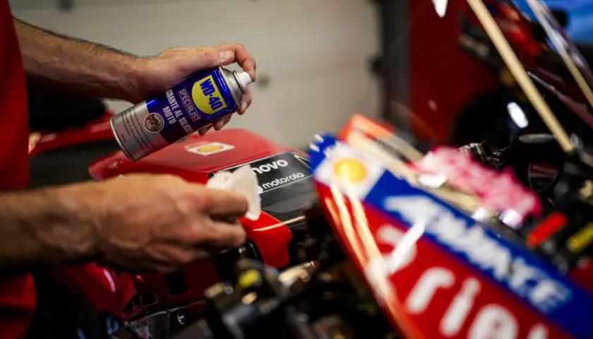 Mani che spruzzano WD-40 su una moto rossa per la lucidatura plastica, in preparazione per la gara.